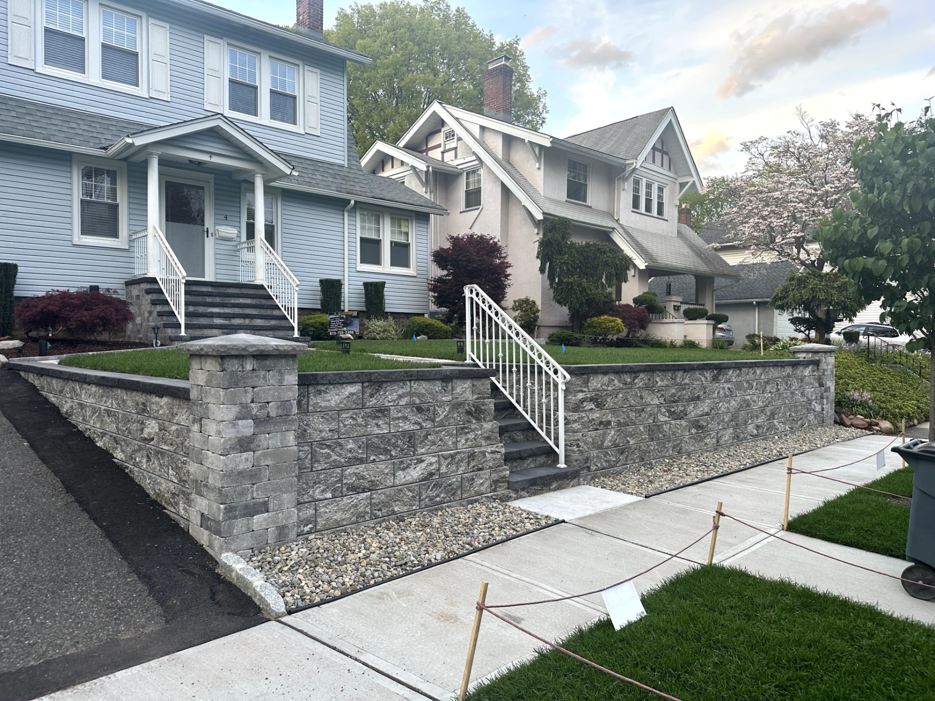 Newly installed concrete sidewalk and stone retaining wall in front of a blue house in Nutley, Essex County, New Jersey