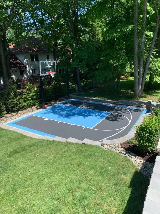 Custom concrete and masonry basketball half-court installation with paver border at a residential backyard in North Caldwell, Essex County, New Jersey by Masonry Pro Construction.