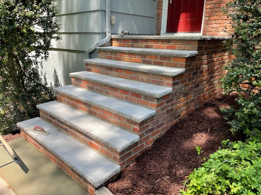 Newly repaired masonry steps with brick and bluestone treads leading to a red door in Caldwell, NJ