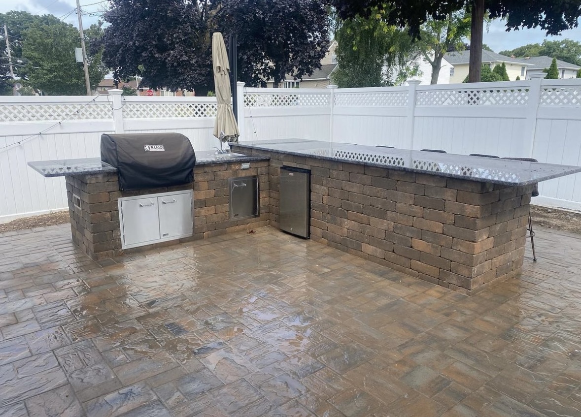 Custom outdoor kitchen with granite countertop, built-in grill, and refrigerator on a stamped paver patio in Fair Lawn, Bergen County, NJ, by Masonry Pro Construction.