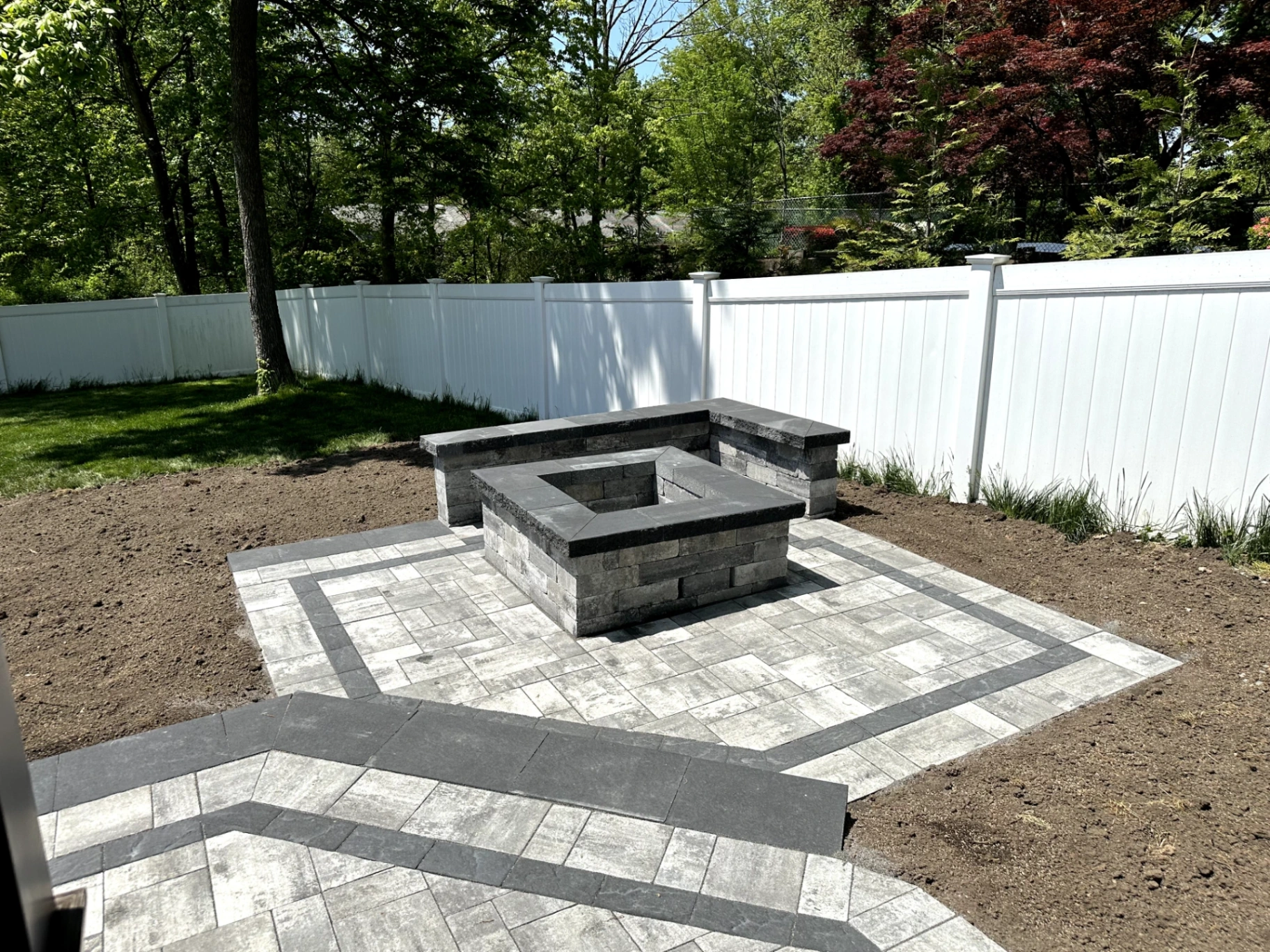 Paver patio with square fire pit and seating wall installation in a backyard in Pine Brook, Morris County, NJ, by Masonry Pro Construction.