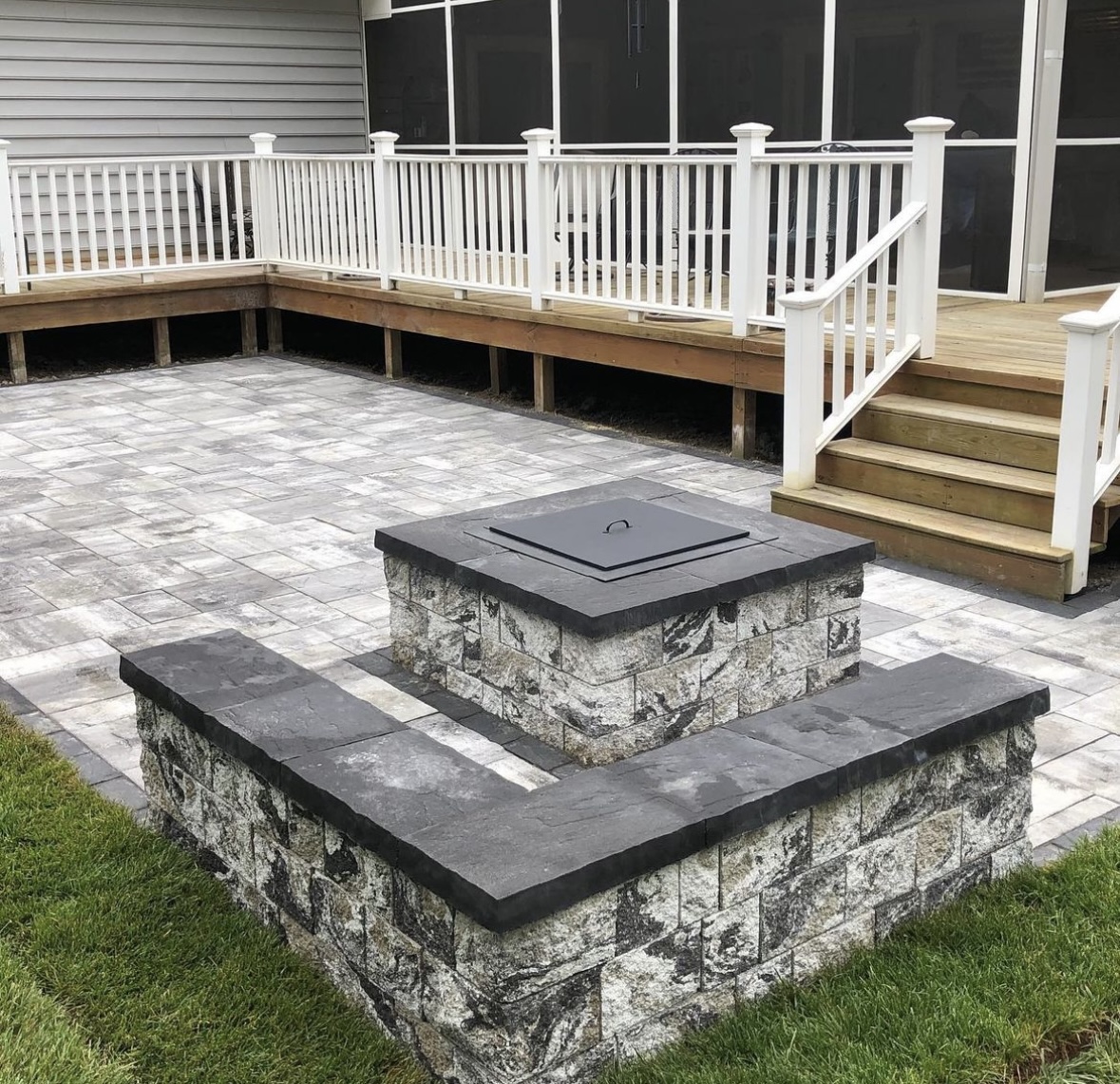 Paver patio with custom stone fire pit and seating wall installed next to a deck in Verona, Essex County, NJ, by Masonry Pro Construction.