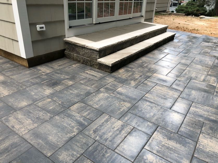 Paver patio with stone-faced steps leading to a back door at a home in Essex Fells, Essex County, NJ, by Masonry Pro Construction.