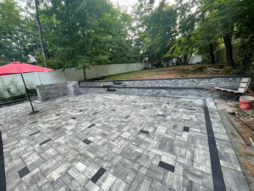 Large paver patio installation with stone retaining wall at a residential property in Teaneck, Bergen County, NJ, by Masonry Pro Construction.