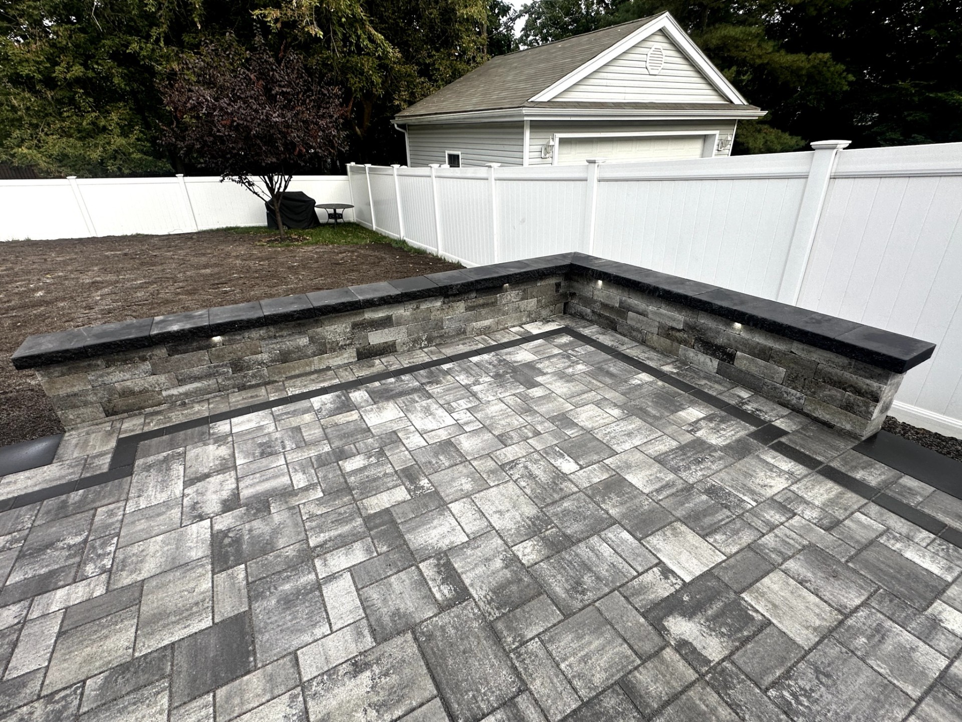 Newly installed patio pavers with a stone retaining wall and white vinyl fence in Verona, New Jersey