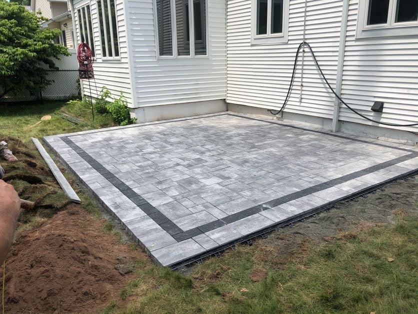 New paver patio with dark border installed behind a white residential home in Bloomfield, Essex County, NJ, by Masonry Pro Construction.