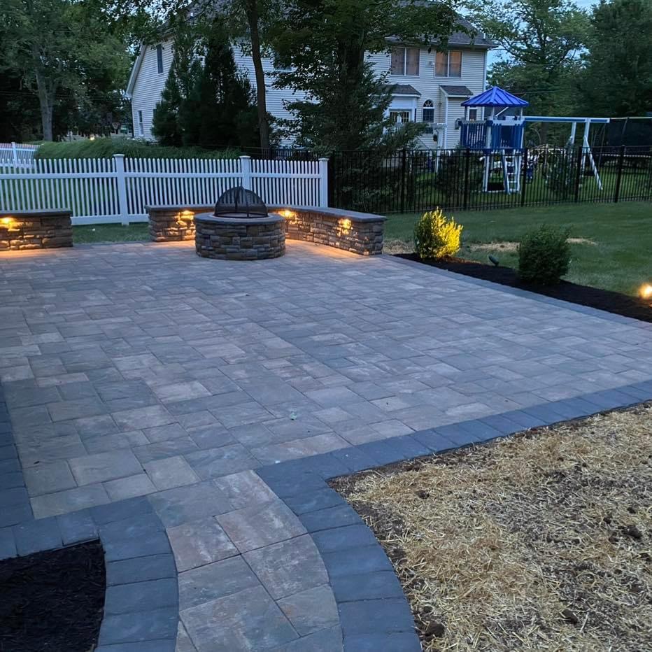 Paver patio with stone fire pit and landscape lighting installed at a backyard in Fair Lawn, Bergen County, NJ, by Masonry Pro Construction.
