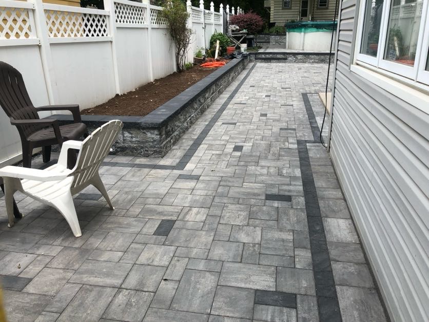 Herringbone pattern paver patio with dark border and stone planter wall installed at a home in Newark, Essex County, NJ, by Masonry Pro Construction.