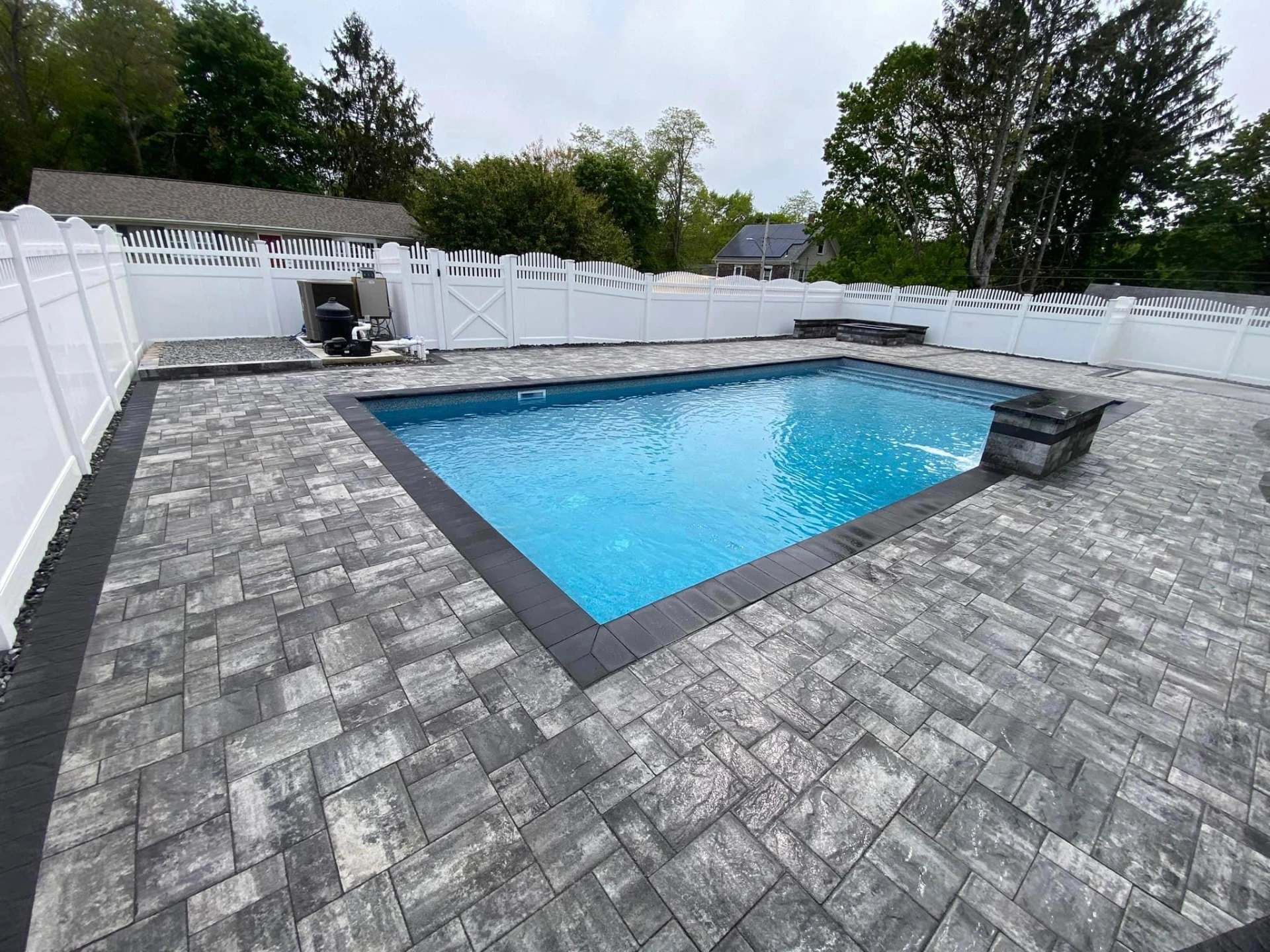 Paver patio surrounding an in-ground pool with dark border and stone fire pit in Wayne, Passaic County, NJ, by Masonry Pro Construction.