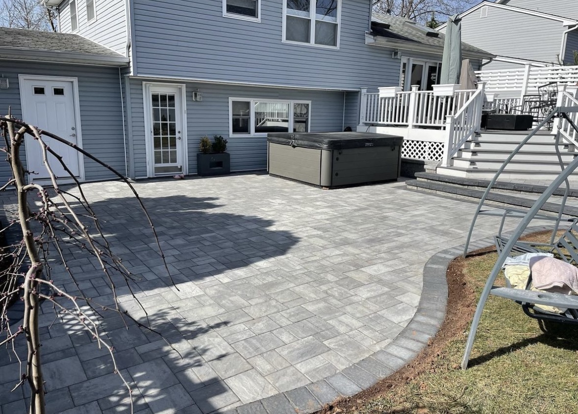 New paver patio with hot tub pad and curved border installed at a blue-sided home in Woodland Park, Passaic County, NJ, by Masonry Pro Construction.
