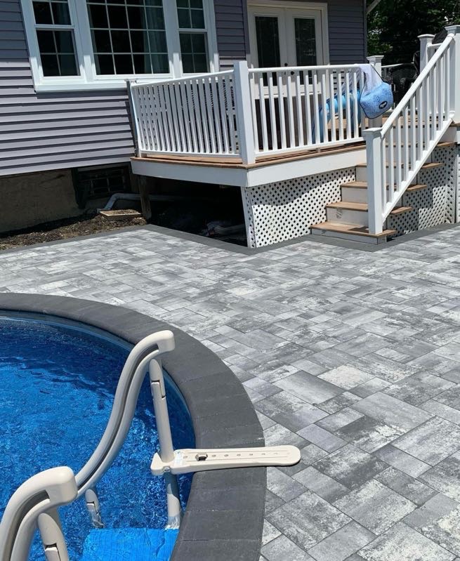 Paver patio installed around an in-ground pool next to a deck at a home in Wayne, Passaic County, NJ, by Masonry Pro Construction.