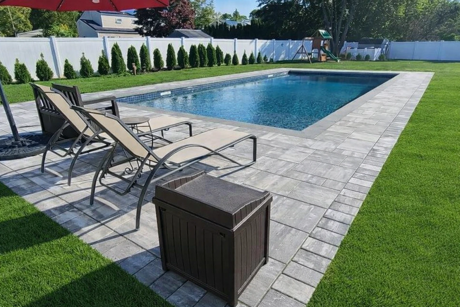 Paver patio surrounding an in-ground pool with lounge furniture in Ridgewood, Bergen County, NJ, by Masonry Pro Construction.