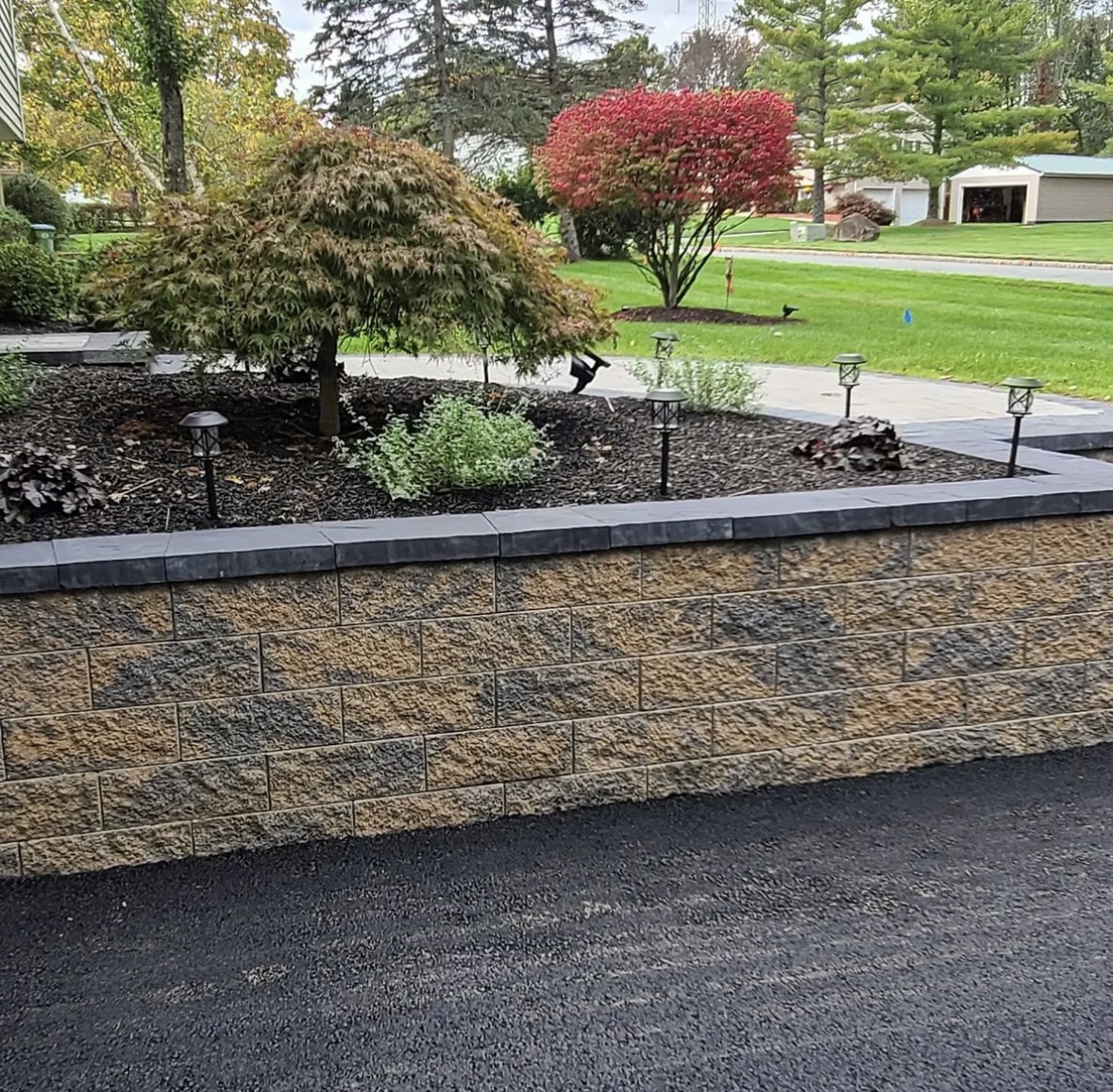 Block retaining wall with dark cap stones and landscaping installed along a driveway in Upper Montclair, Essex County, NJ, by Masonry Pro Construction.