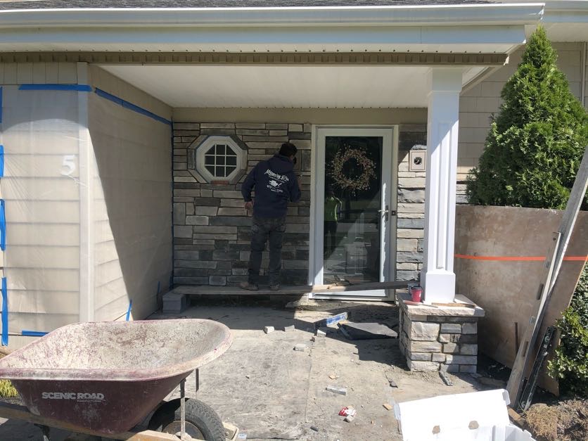 Mason working on stone veneer installation around a front door in West Caldwell, Essex County, New Jersey